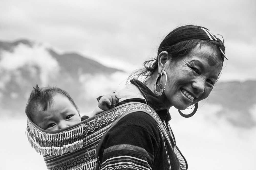 Black and white Travel photography of a smiling woman carrying her baby in Vietnam.